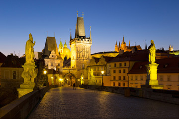 Fototapeta na wymiar Night colorful Prague gothic Castle with St. Nicholas' Cathedral and Bridge Tower from Charles Bridge with its baroque Statues without People at the time of Coronavirus, Czech Republic