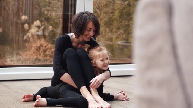 Straight beautiful mother and daughter in black costumes are doing gymnastics together. The happy family are having fun in the modern house . The family is stayng healthy during quarantine doing