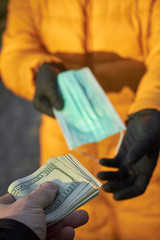 Hands exchange 100 dollar bills for a surgical face mask signifying a spike in price of face mask...