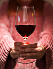 A woman wearing a pink sweater holds a glass of red wine