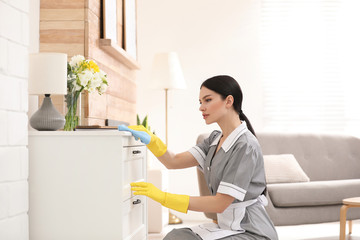 Young chambermaid wiping dust from furniture in hotel room