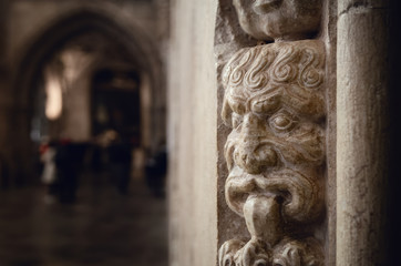 Ancient portuguese manueline late gothic decoration on a church wall, with a stone mask in foreground and the church nave blurred in background