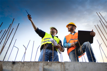Men in hardhat and yellow and orange jacket posing on building site