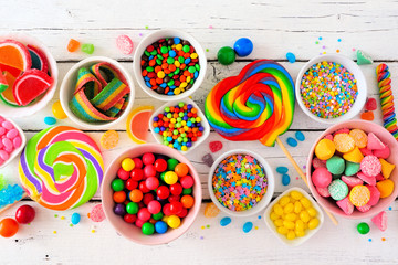 Colorful sweet candy buffet table scene. Top view over a white wood background.