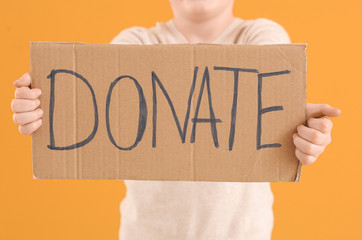 Little boy holding cardboard with text DONATE on color background