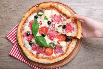 Woman taking piece of delicious pizza Diablo at wooden table, closeup
