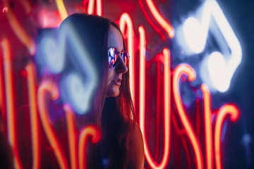 a girl in neon light with glasses in smoke near a nightclub. City street in neon light. Fashion...