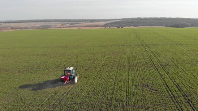 Tractor spreading artificial fertilizers in green field. Farmer fertilizing arable land with nitrogen and potassium fertilizer.