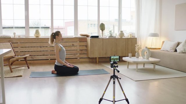 Attractive Caucasian recording making live stream or vlog about doing yoga at home. Stay home, quarantine workout. Shot on ARRI Alexa Mini with Cooke S4 lenses