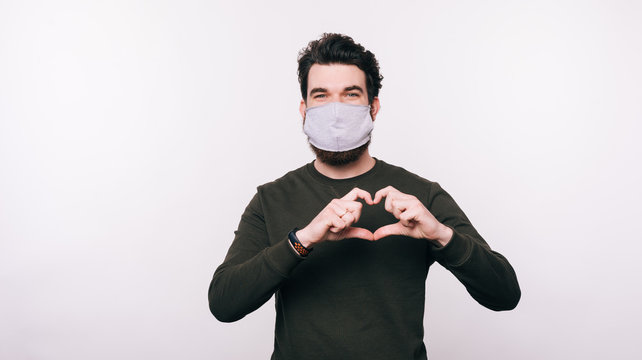 Photo Of Man With Facial Mask Making Heart Love Gesture Over White Background.