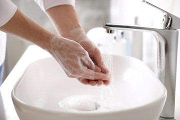 Man washing hands with soap over sink in bathroom, closeup