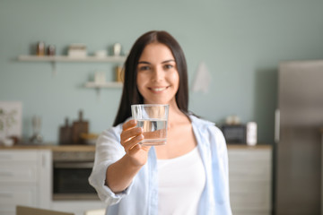 Beautiful young woman drinking water in kitchen