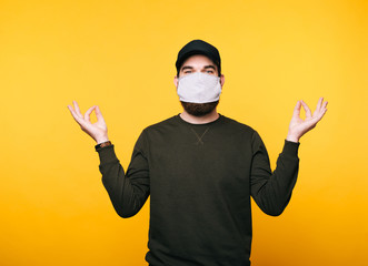 Portrait of young man with facial mask doing yoga over yellow background