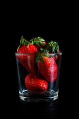 RED STRAWBERRIES IN GLASS CUP ON BLACK BACKGROUND