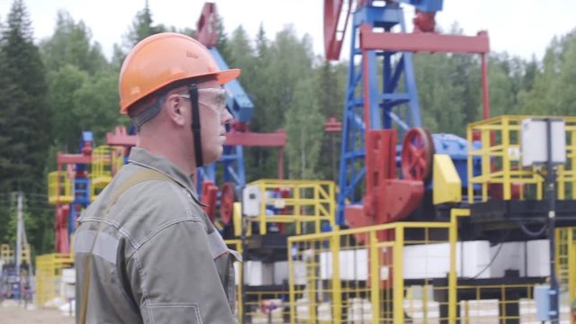 Slow motion shot of oil worker walking near oil pump jacks in oil field. Balancing drive rod pumps oil rocker. Pumping crude oil for fossil fuel energy with drilling rig in oil field.