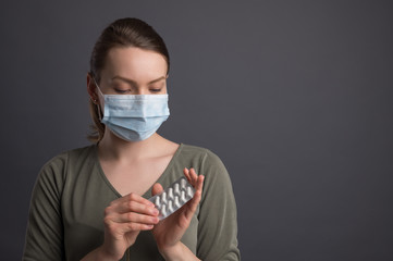 Pharmacology.Girl in a mask from coronavirus holds pills, medicine for coronavirus.On a gray background, for media headlines, news, newspapers