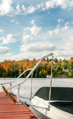 Boat moored to wooden dock, cottage country, autumn foliage across the lake.