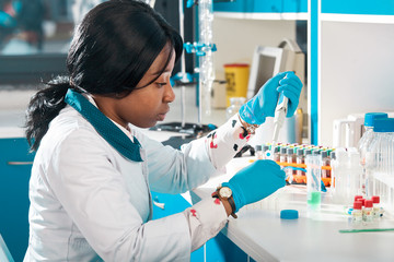 African scientist or graduate student in lab coat and protective wear performs RT-PCR testing in...