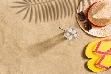 Fototapeta na wymiar Top view straw hat, sunglasses and glass of water with copy space. Traveler accessories on sand. Travel vacation concept. Summer background. Harsh light with shadows