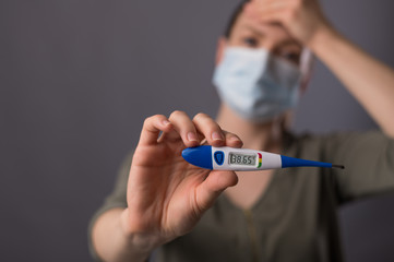 High temperature, symptom of the corona of the virus. A girl in a mask holds a termometer with a high temperature. media, newspaper or news. Symptoms, the danger of high temperature with the virus