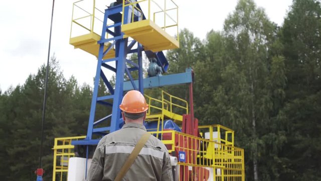 Oil field technical worker overseeing site of crude oil production. Industrial oil pump jack working and pumping crude oil for fossil fuel energy with drilling rig in oil field.