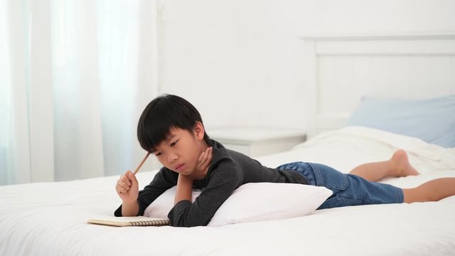 4k Young Asian boy lay on a bed and get an idea to solve a problem for his homework in a book