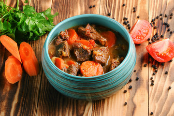 stew made with beef, potatoes, carrots and herbs on wooden background and ingredients