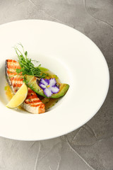 plate of grilled salmon steak with avocado closeup on cement background