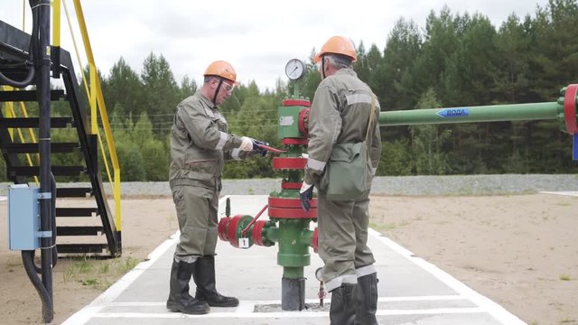 Oil field technical workers opening or closing valve of wellhead. Injection tree is destined for injection wells sealing and their operating regime regulation. Oil industry