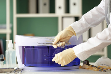 Doctor putting medical instruments into ultraviolet sterilizer in clinic