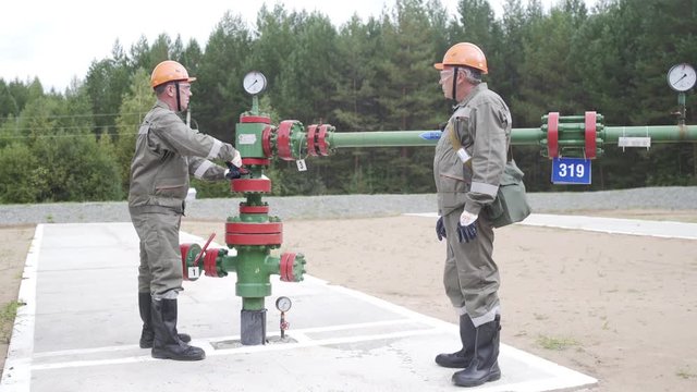 Oil field technical workers opening or closing valve of wellhead. Injection tree is destined for injection wells sealing and operating regime regulation. Experienced mentor teaching young specialist
