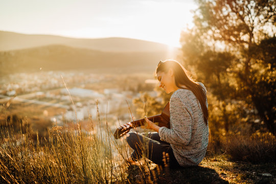 Young guitarist playing acoustic guitar and enoying the sunset.Learning to play an instrument.Singer-songwriter in nature searching for inspiration in nature.Musical therapy.