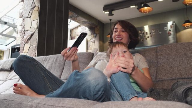 Pretty mother and her son are laying on a counch in a modern house isolated.