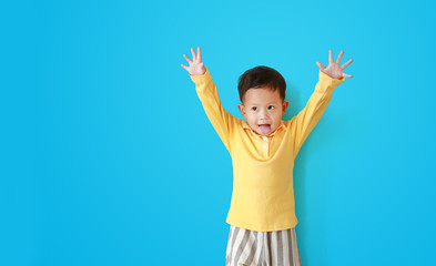 Portrait of funny asian baby boy playing peekaboo with showing stick out tongue isolated on blue background with looking beside with copy space.