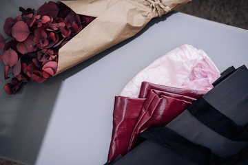 Black shopping bag with pink leather cloth, red dried eucalyptus bouquet wrapped in brown craft paper. Fashion, beauty bloogging concept, minimalism