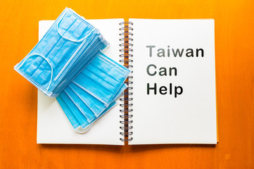 epidemic healthcare concept ,Taiwan Can Help text written on a notebook .,Alcohol spray and face mask on wooden background