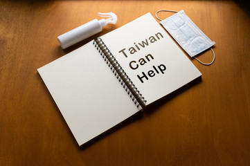 epidemic healthcare concept ,Taiwan Can Help text written on a notebook .,Alcohol spray and face mask on wooden background