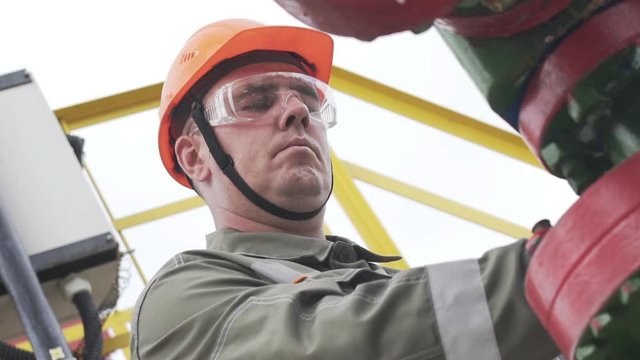 Slow motion of oil field technical worker overseeing site of crude oil production. Industrial oil pump jack working and pumping crude oil for fossil fuel energy with drilling rig in oil field