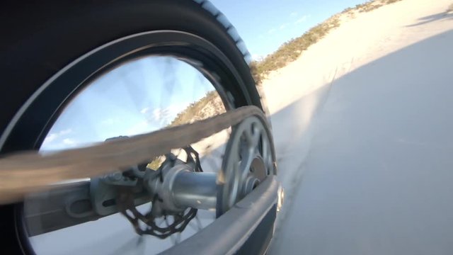 Shot from action camera mounted on the rear swingarm of a dirt motorbike moving on sand dunes. Motocross bike moving in desert.
