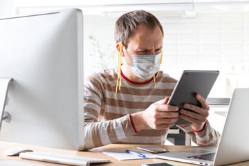 Man in face mask with noodles on his ears, reads fake/breaking news and a speech by the president on tablet about coronavirus during self-isolation, quarantine. Desinformation, lies in social media