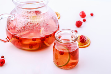 Healthy hot fruit drink. Fruit hot tea with the addition of oranges, lemons and raspberries in a glass cups and teapot on a white table.