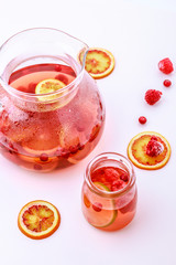 Healthy hot fruit drink. Fruit hot tea with the addition of oranges, lemons and raspberries in a glass cups and teapot on a white table.