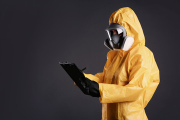 Woman in chemical protective suit holding clipboard on grey background, space for text. Virus...