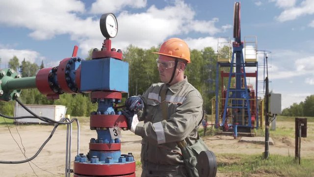 Oilman in orange helmet and protective glass closing valve of x-mass wellhead to shut off well. Decline in oil production after adoption of agreements at meeting of OPEC to stabilize price of oil.