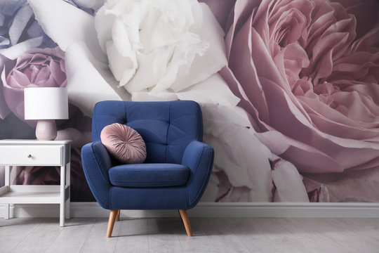 Comfortable armchair near wall with floral wallpaper. Stylish living room interior