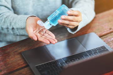 Closeup image of a woman using and applying alcohol gel to clean hands while working on laptop at home for Healthcare and Covid-19 concept