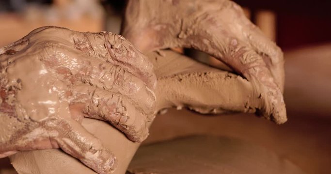 Young handsome sculptor tears wet clay with his hands. Artisan potter prepares material for his pottery. Strong male hands squeeze wet ceramic for modeling and sculpting. Work close-up.