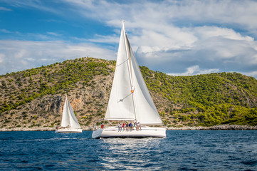 Fototapeta na wymiar two sailing yachts with white sails floating on the sea among the rocks