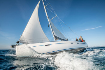 One white sailing yacht floats on the sea with waves and spray. The view from the side - obrazy, fototapety, plakaty