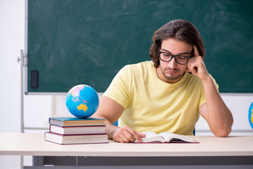 Young male geography teacher in front of blackboard